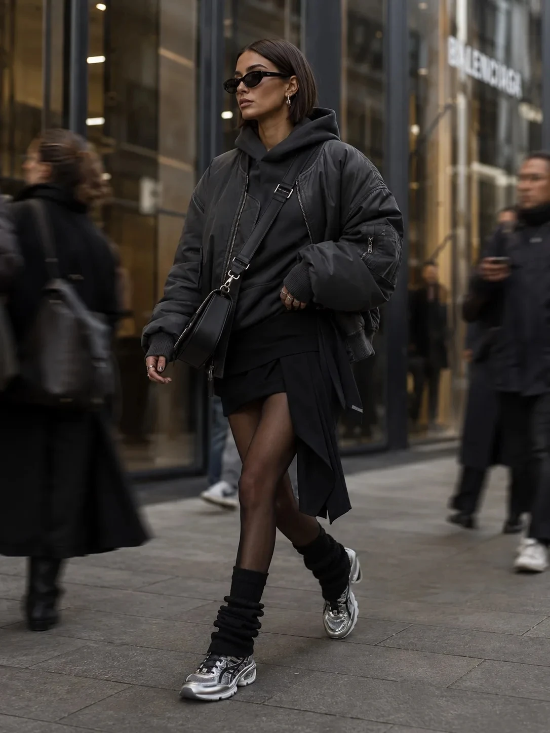 high-fashion editorial street style scene in a modern luxury shopping district, oversized charcoal bomber jacket - изображение